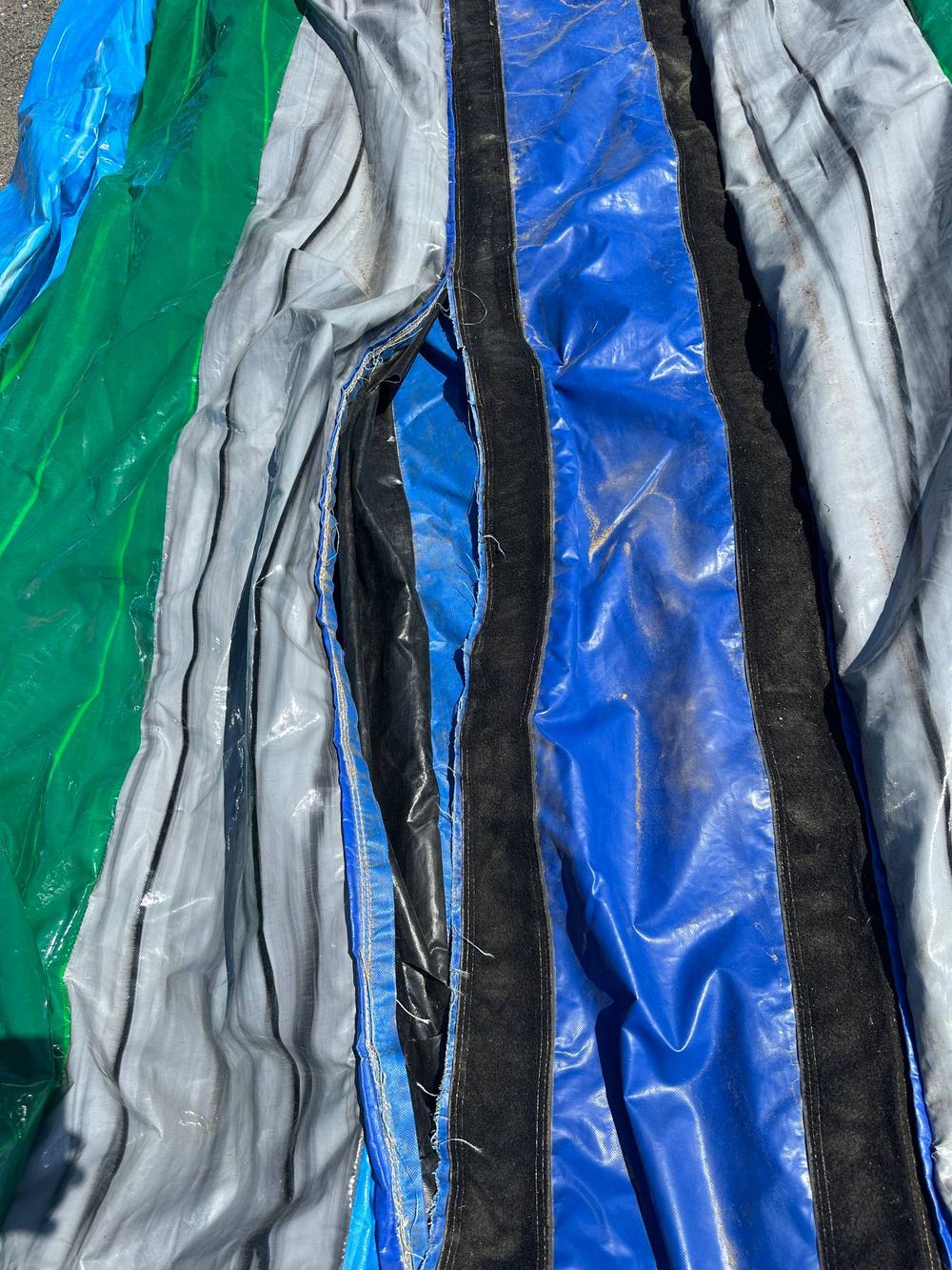Before photo of a torn seam on a green and blue water slide panel near the entrance, completed by Stitches For Bounces