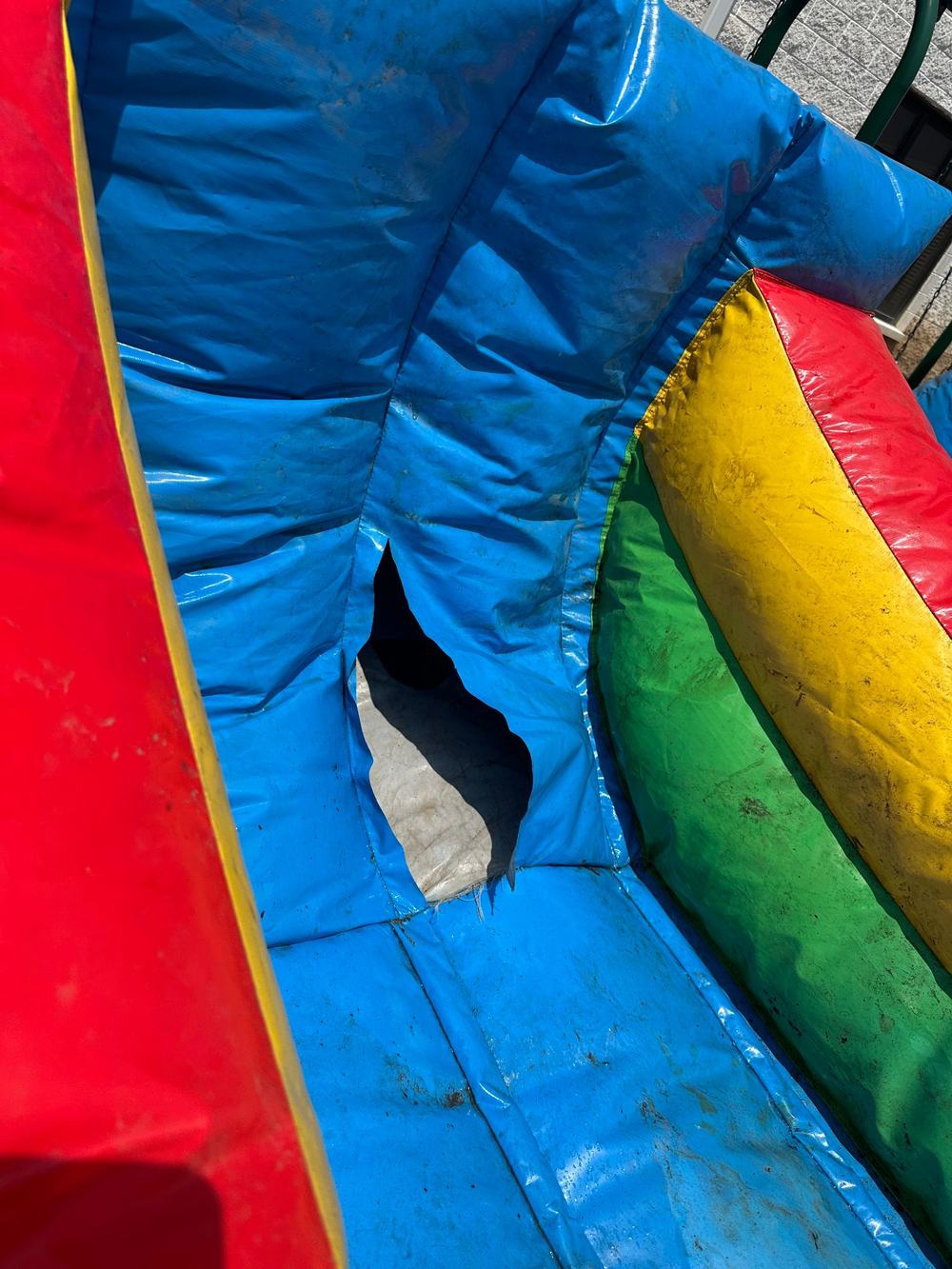 Before photo of a torn seam near the base of a colorful inflatable water slide, completed by Stitches For Bounces