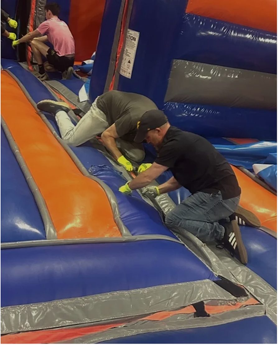 Repair class students working together on a blue and orange inflatable slide during hands-on training