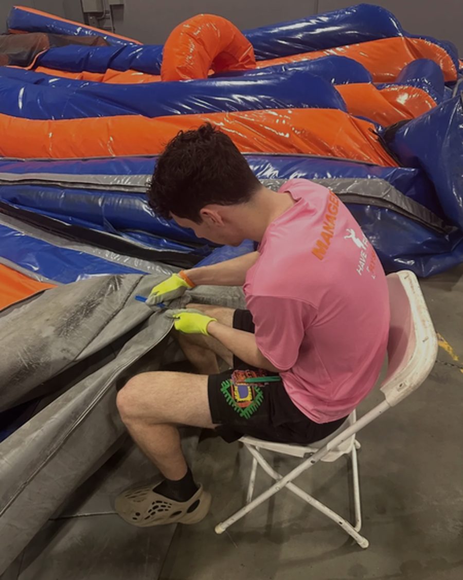 Bounce Repair University student sewing a torn seam on an orange and blue inflatable during a hands-on class