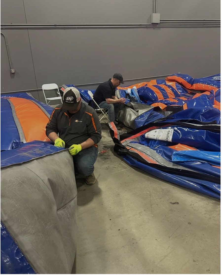 Two Bounce Repair University students repairing inflatable panels side by side in the training warehouse